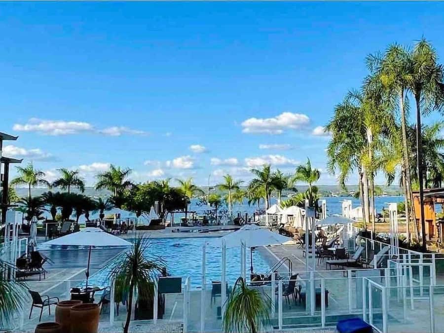 Zona de piscina con sillones reclinables y palmeras, con vista a una masa de agua.