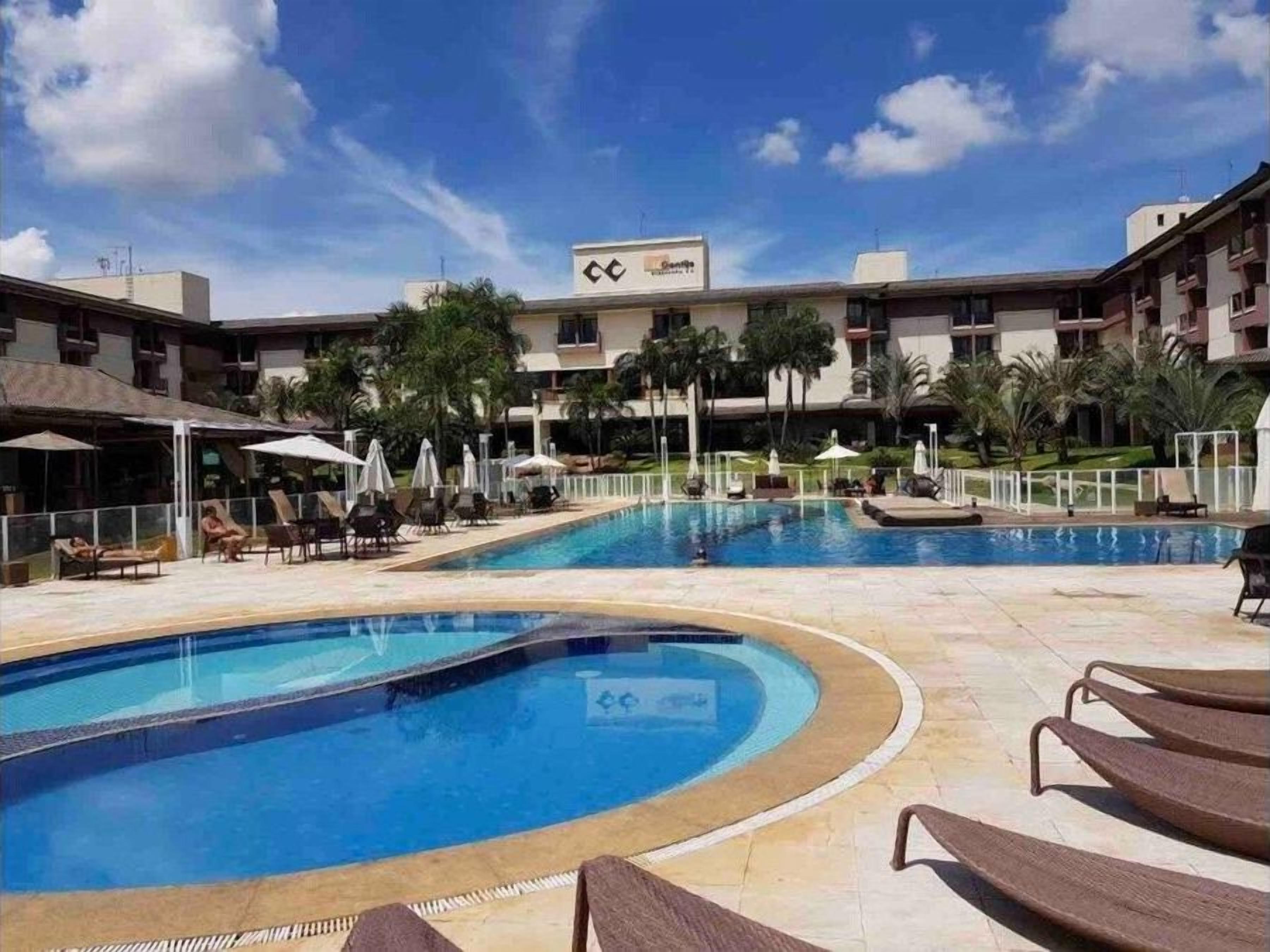 Un hotel con piscina, sillas de descanso y palmeras.