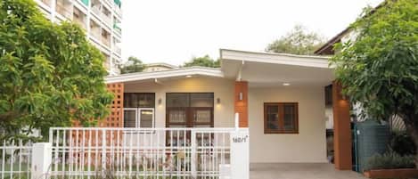 Edificio residencial con entrada cubierta, camino de acceso con portón y un pequeño jardín.