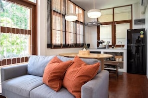 A living room with a sofa, a dining table, and a kitchen area with a refrigerator.