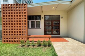 Entrada de un edificio con cercado de madera, un banco y un pequeño jardín.