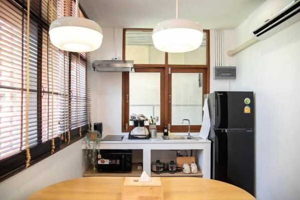 A kitchen with a wooden table, two pendant lights, a black refrigerator, and a window with blinds. - Ray's Home,3Br with Front Yard,Walkable to Nimman (Chiang Mai)