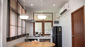 A compact kitchen with a dining table, a refrigerator, and a window with blinds. - Ray's Home,3Br with Front Yard,Walkable to Nimman (Chiang Mai)