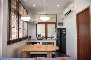 A compact kitchen with a dining table, a refrigerator, and a window with blinds. - Ray's Home,3Br with Front Yard,Walkable to Nimman (Chiang Mai)