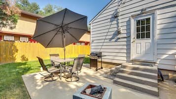A patio with a table and chairs, a large umbrella, and a fire pit.