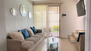 Un salon avec un canapé beige, une table basse en verre et un téléviseur fixé au mur.