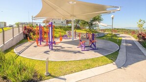 Un espace de remise en forme extérieur équipé d’appareils d’exercice, doté d’un auvent ombragé et d’un chemin pavé.
