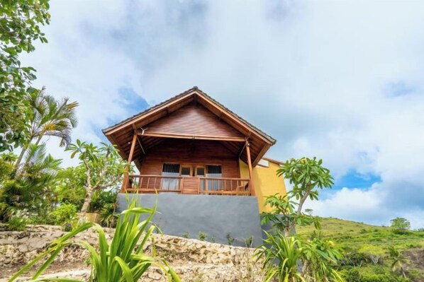 A single-story building with a sloped roof, a balcony, and a view of a hilly landscape.