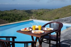 A dining table with plates of food and drinks by a pool with a view of the ocean. - Nusa Penida Pini Sentana (Bali)