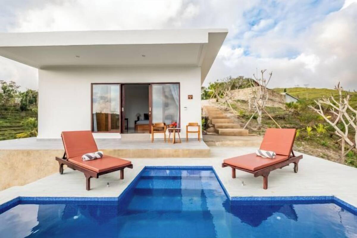 A modern pool area with two lounge chairs, a clear blue pool, and a building with a glass door entrance.