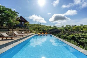 A swimming pool with lounge chairs and a house in the background. - Nusa Penida Pini Sentana (Bali)