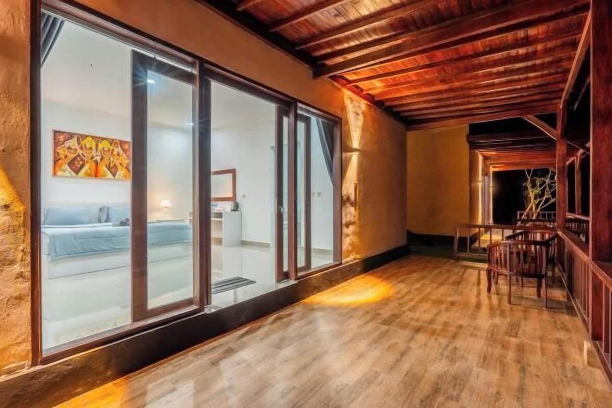 A room with a wooden ceiling, a large sliding glass door leading to a bedroom, and a seating area with chairs.