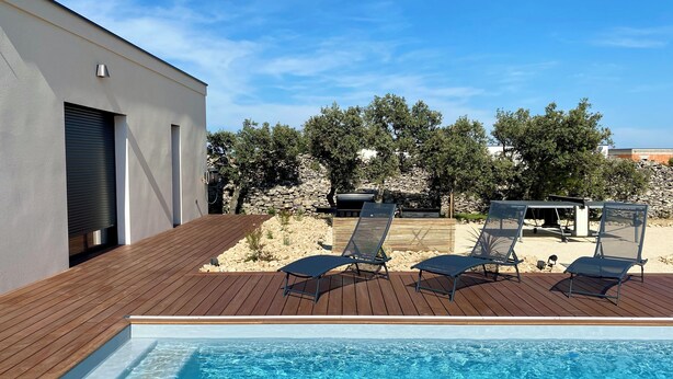 Una piscina con lettini, un pontile in legno e un muro di pietra sullo sfondo.