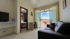 A living room with a sofa, a TV, a desk, and a bed. - 2 suítes térreo - próximo da piscina (Aquiraz)