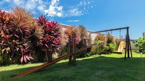 A backyard with a swing set, lush green grass, and various plants. - 2 suítes térreo - próximo da piscina (Aquiraz)