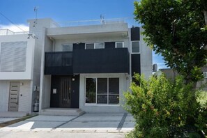 A modern two-story building with a flat roof, a balcony, and a large sliding glass door.
