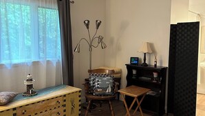 Una sala de estar acogedora con suelo de madera, una silla de madera con un cojín decorativo, una mesita con una lámpara y una estantería.