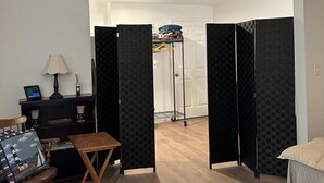 Una habitación con suelo de madera, un escritorio con lámpara, una silla, una cama y un armario.