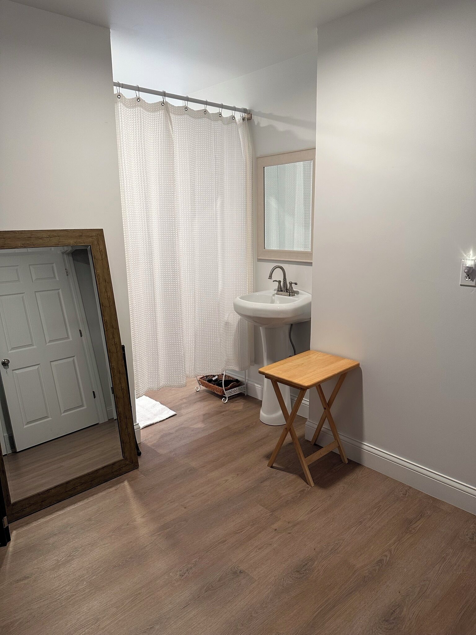 Un baño con suelo de madera, un lavabo blanco, un espejo y una cortina de ducha.
