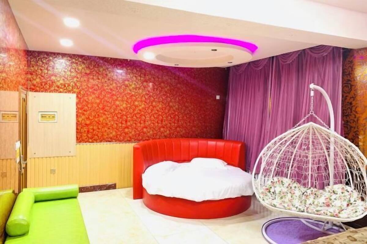 A room with a red sofa bed, a hanging chair, and a patterned wall.