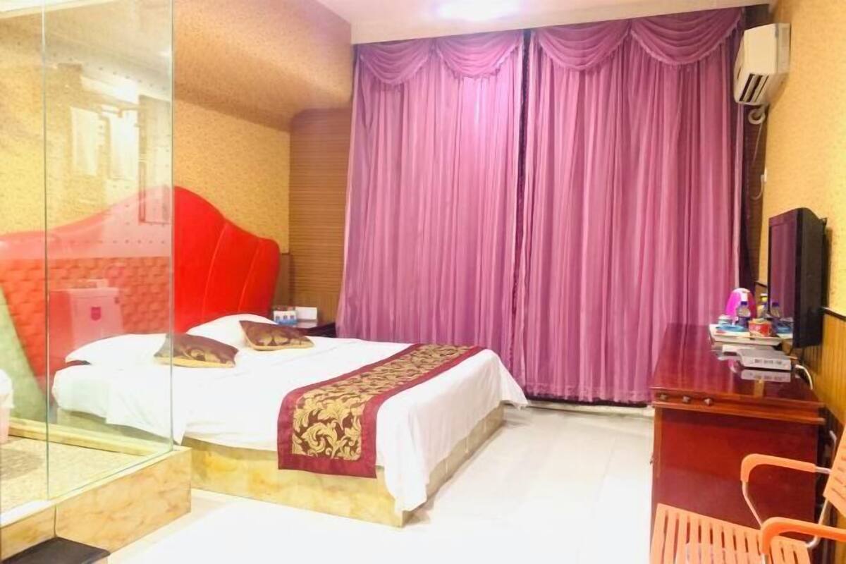 A hotel room with a bed, a desk, a chair, and a large window with curtains.