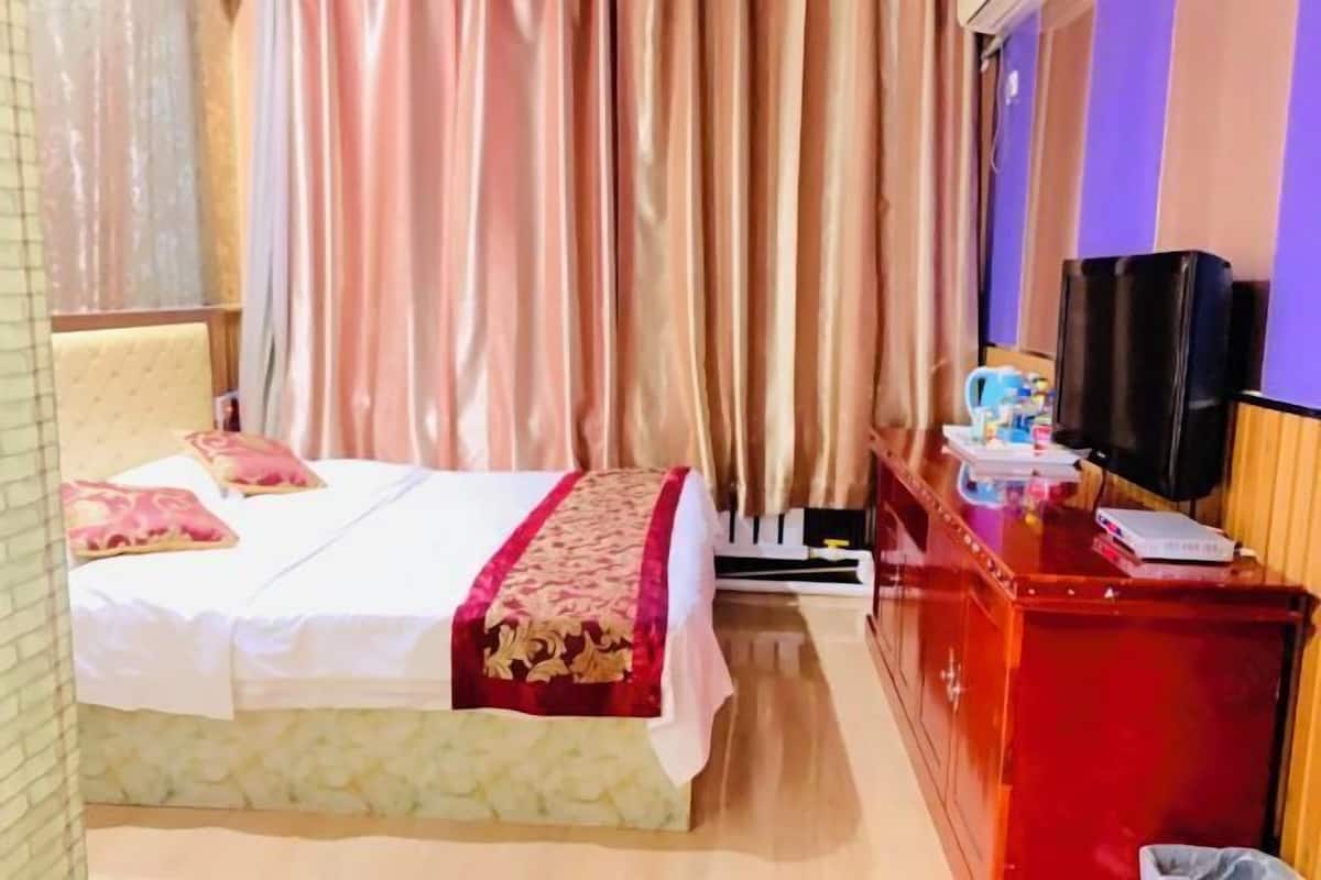 A hotel room with a bed, a desk with a television, and curtains.