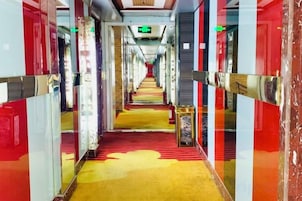 Un pasillo de hotel con alfombra roja, paredes espejadas y una escalera central.