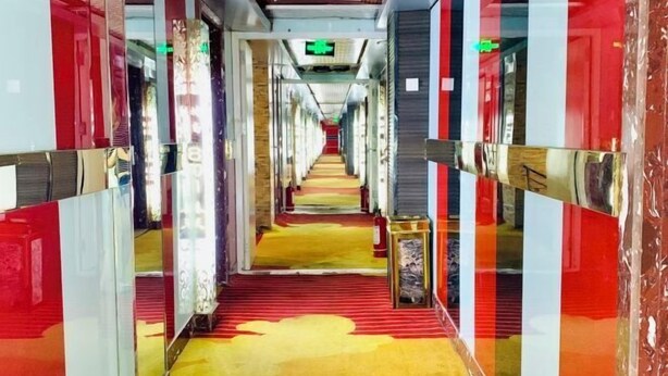 A hotel corridor with mirrored walls, a red carpet, and a fire extinguisher on a table. - Suihua Fashion Spring Express Hotel (Suihua)