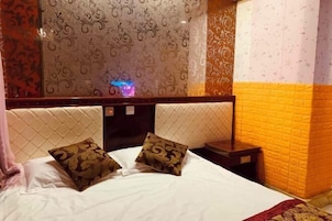 Habitación de hotel con cama, dos almohadones decorativos, una mesita de noche y un papel tapiz con motivos.