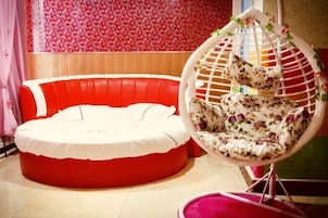Um sofá redondo vermelho, uma cadeira suspensa com padrão floral e uma parede com papel de parede floral vermelho.