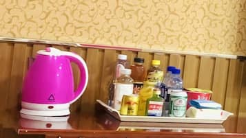 A wooden table with a pink kettle and a tray containing various items like bottles, cans, and boxes.