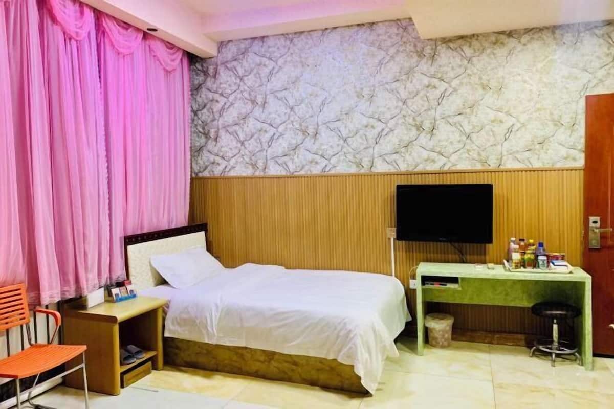 A hotel room with a bed, a desk, a chair, a television, and a wardrobe.