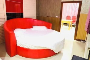 A circular red bed in a room with a wooden door and a table with chairs in the background.