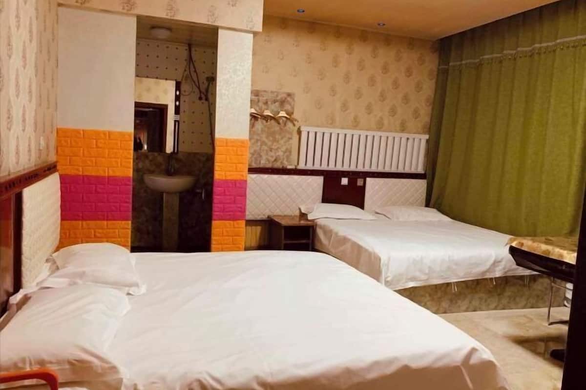 A hotel room with two beds, a bathroom with a sink, and a radiator.