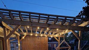 A wooden deck with a pergola, string lights, wicker furniture, and a hanging chair. - Spacious 4-bedroom house in charming Des Plaines with AC, WiFi (Des Plaines)