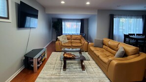A living room with a brown leather sofa, a coffee table, and a TV mounted on the wall. - Spacious 4-bedroom house in charming Des Plaines with AC, WiFi (Des Plaines)