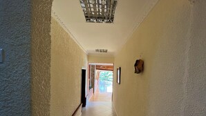 Un corridoio con pareti strutturate, una ringhiera in legno e un pavimento piastrellato che conduce a un'area aperta con vista sul verde circostante.