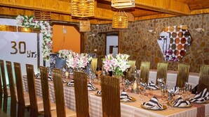 Una sala da banchetto con lunghe tavole imbandite per un evento formale, caratterizzata da tovaglie a righe, sedie dorate e composizioni floreali al centro.
