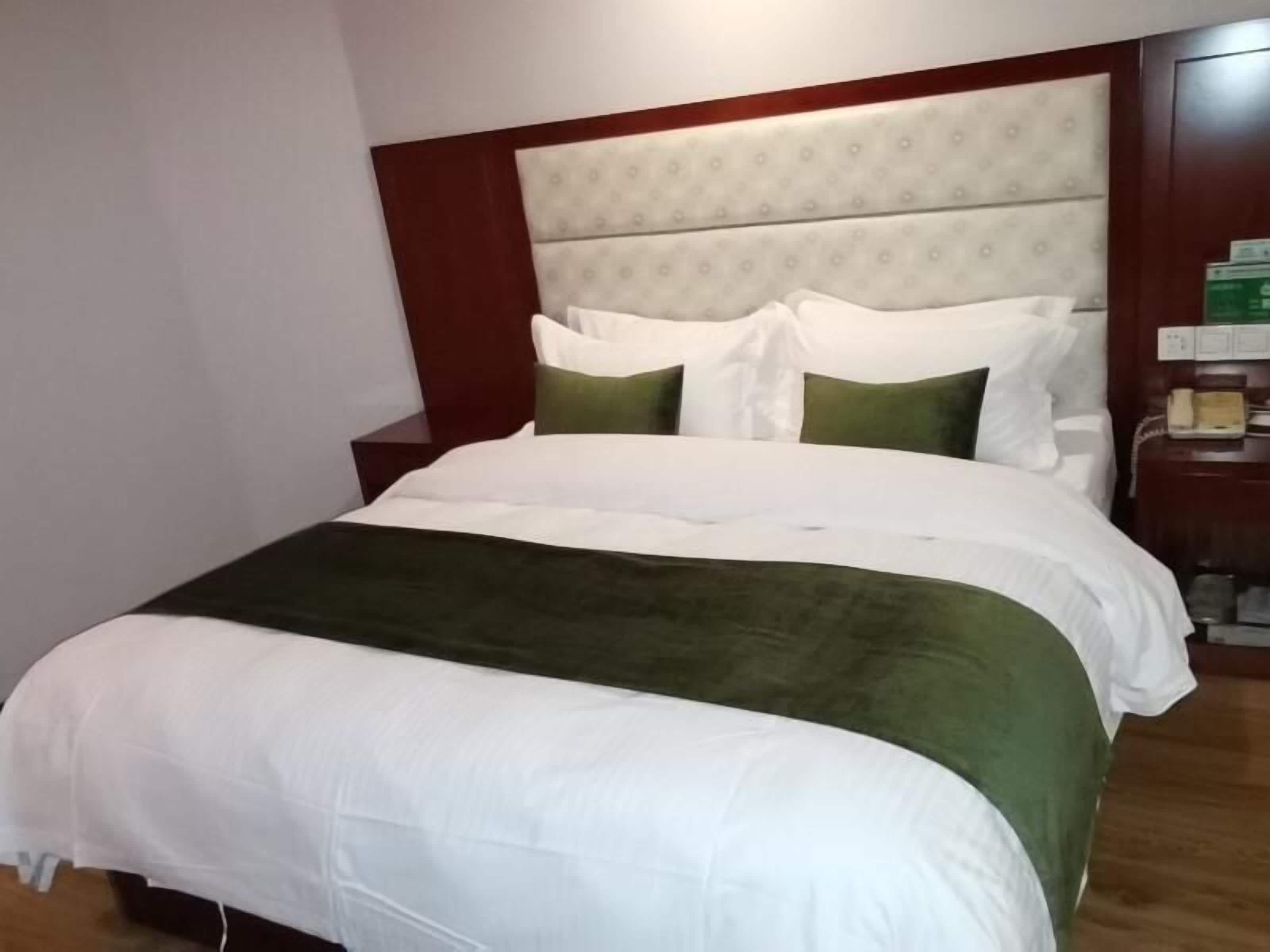 A neatly made bed with a white and green bedspread, a wooden headboard, and a bedside table with a telephone and a green box.