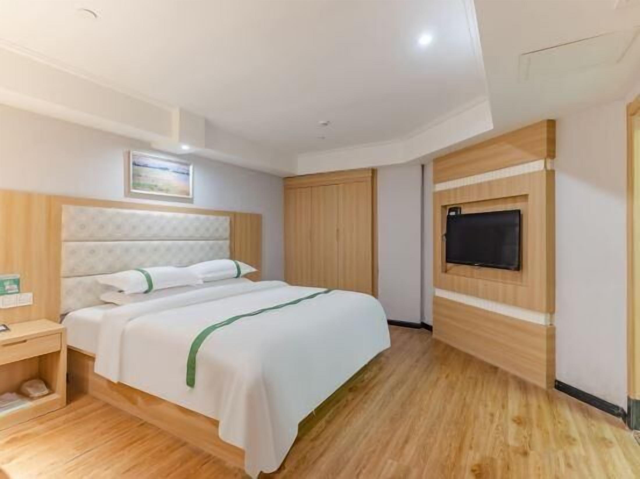 A hotel room with a bed, a bedside table, a TV mounted on the wall, and a wooden floor.