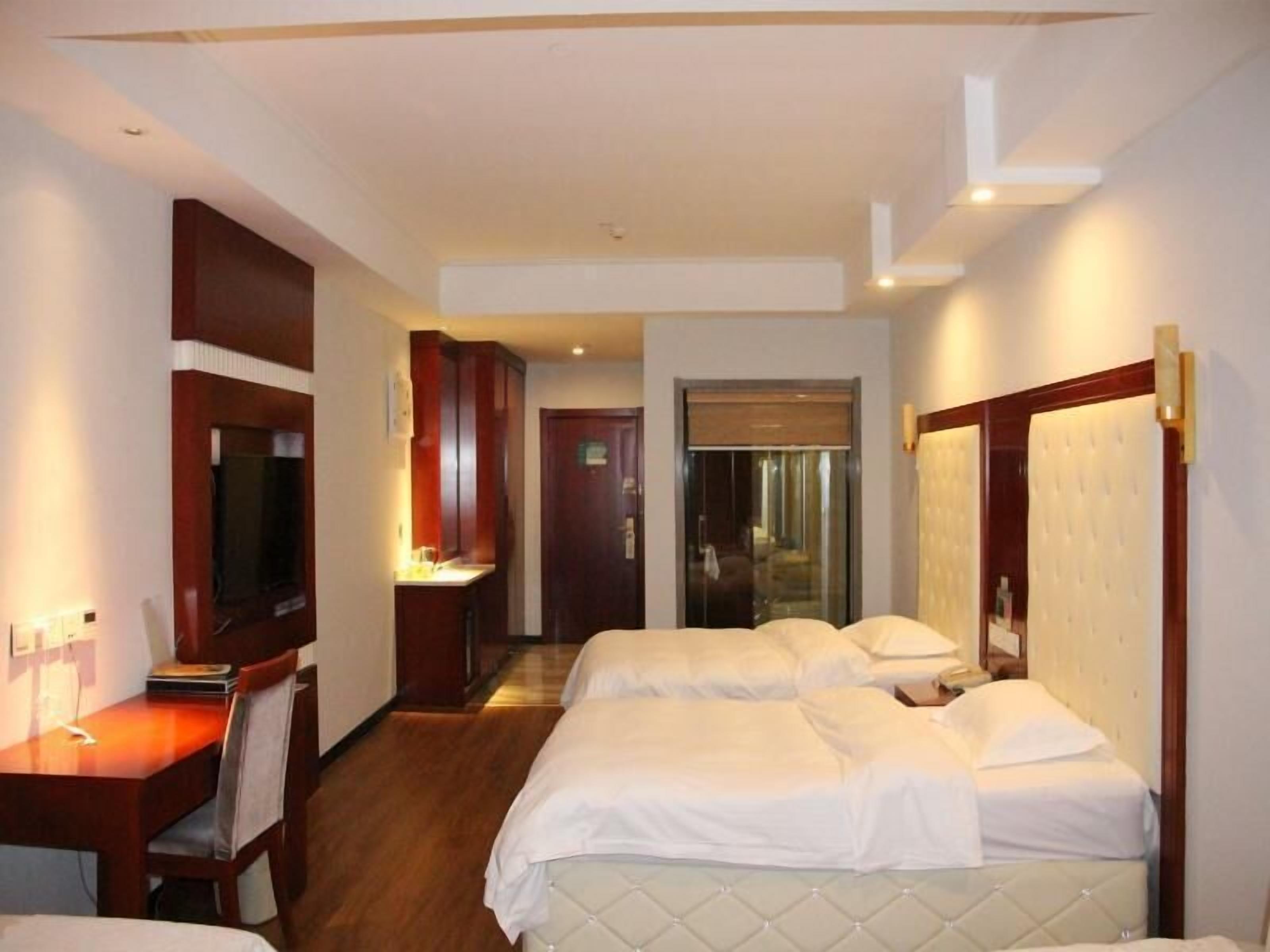 A hotel room with two beds, a desk, a chair, a television, and a bathroom door.
