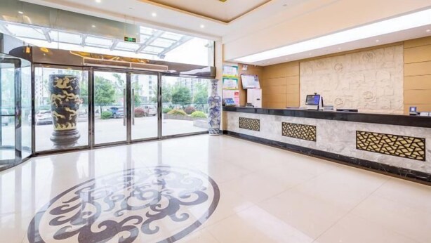 Un vestíbulo de hotel con una recepción, un gran jarrón decorativo y un diseño de piso estampado.