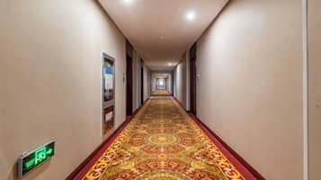 A hotel hallway with a patterned carpet, directional signs, and doors on either side.