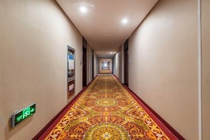 Un pasillo de hotel con alfombra estampada, señales de orientación y puertas a ambos lados.