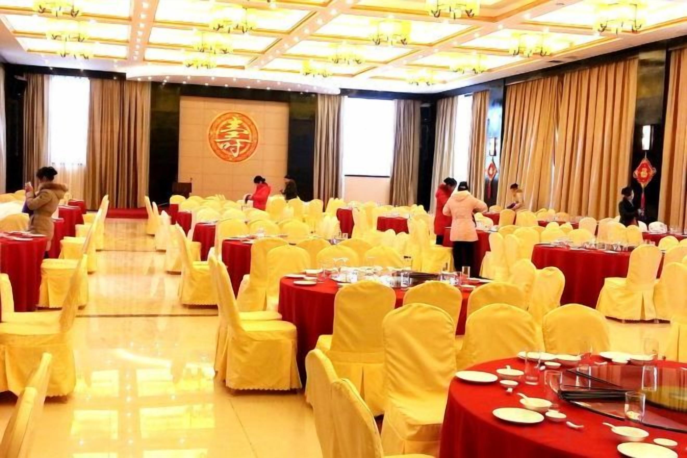A banquet hall with round tables, yellow chairs, and red tablecloths.
