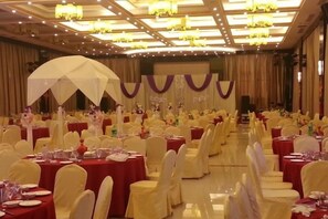 Une salle de banquet avec des tables rondes, des chaises et une scène.