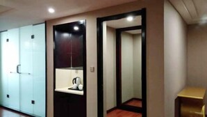 Habitación de hotel con un armario grande, una kitchenette pequeña con hervidor y un espejo.