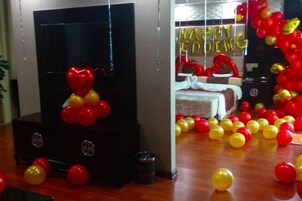 A room with a bed, a TV, and a wall with balloons.