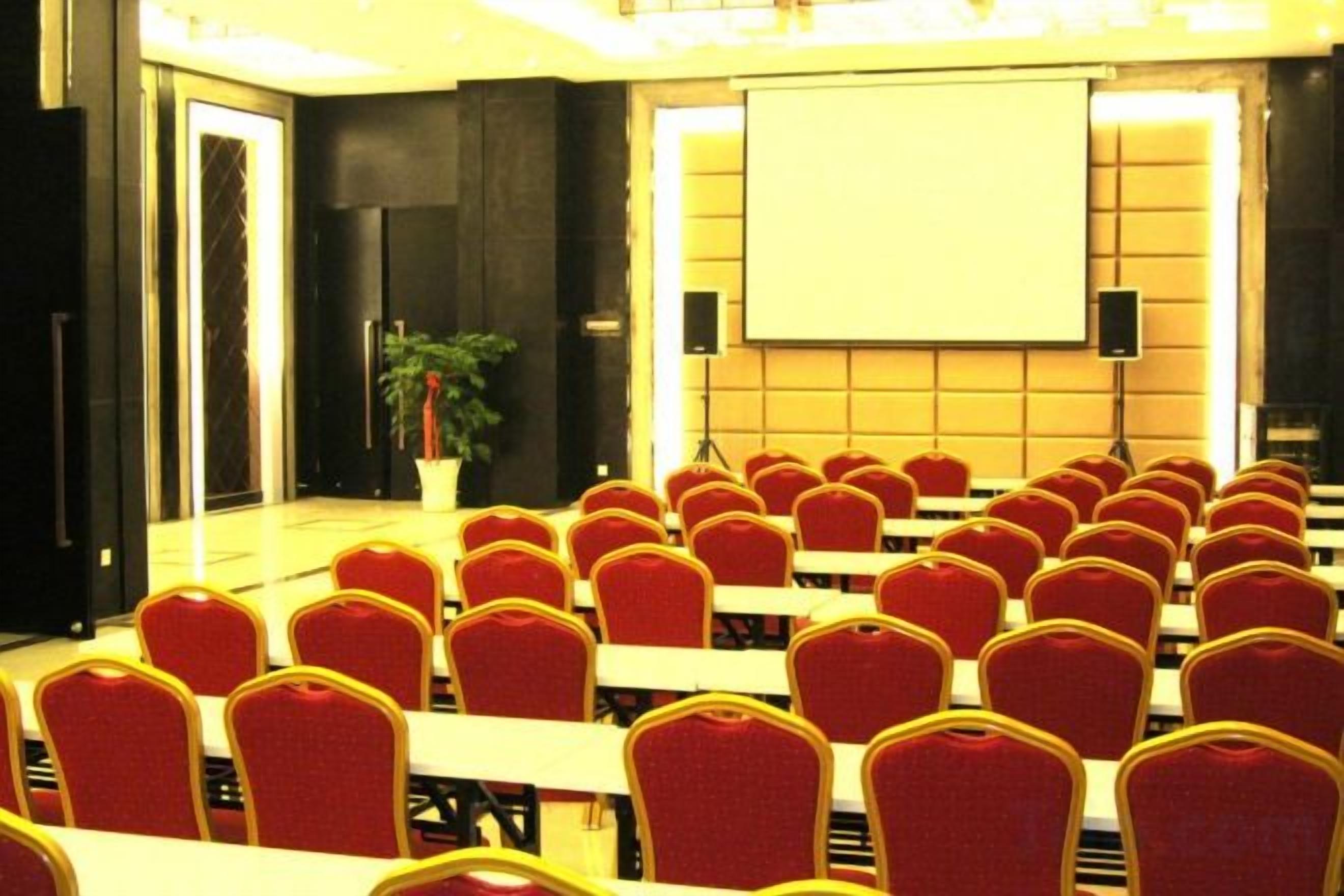A conference room with rows of red chairs, a projector screen, and a potted plant.