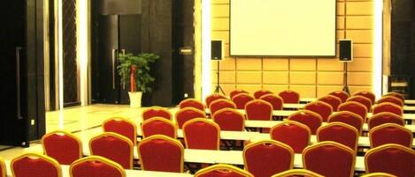 A conference room with rows of red chairs, a projector screen, and a potted plant.
